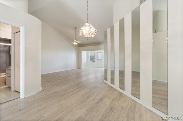 spare room featuring ceiling fan with notable chandelier, light wood-type flooring, and lofted ceiling