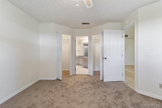 unfurnished bedroom featuring ceiling fan, a spacious closet, ensuite bathroom, light carpet, and a closet