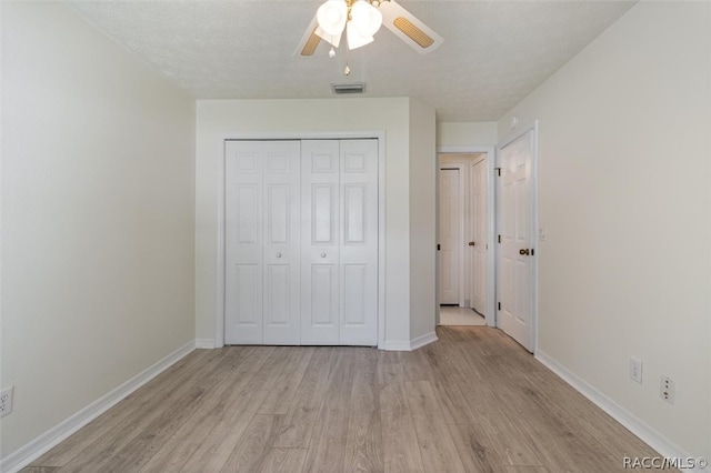 unfurnished bedroom with ceiling fan, a closet, light hardwood / wood-style floors, and a textured ceiling