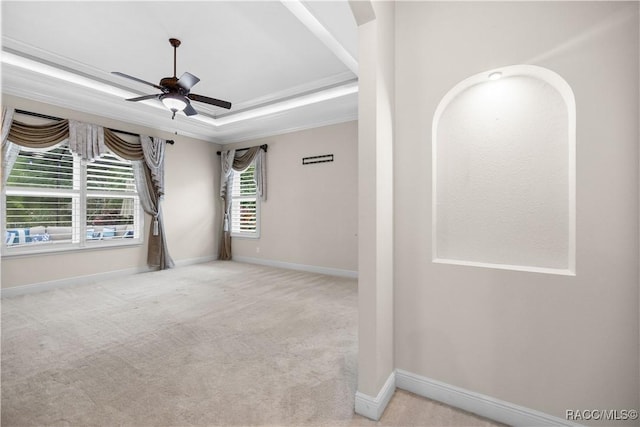 empty room with crown molding, ceiling fan, a tray ceiling, and light carpet