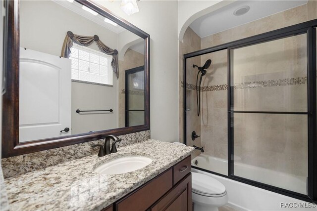 full bathroom featuring vanity, combined bath / shower with glass door, and toilet