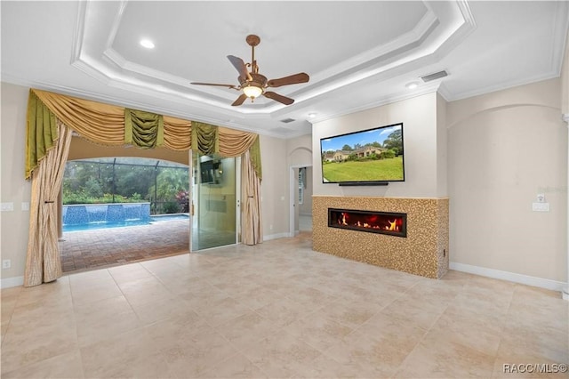 unfurnished living room featuring a raised ceiling, ornamental molding, and ceiling fan