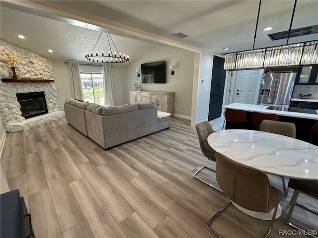 living room with a stone fireplace, a chandelier, a textured ceiling, and light wood-type flooring