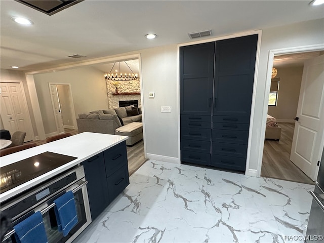 kitchen featuring a stone fireplace, a chandelier, light wood-type flooring, and appliances with stainless steel finishes