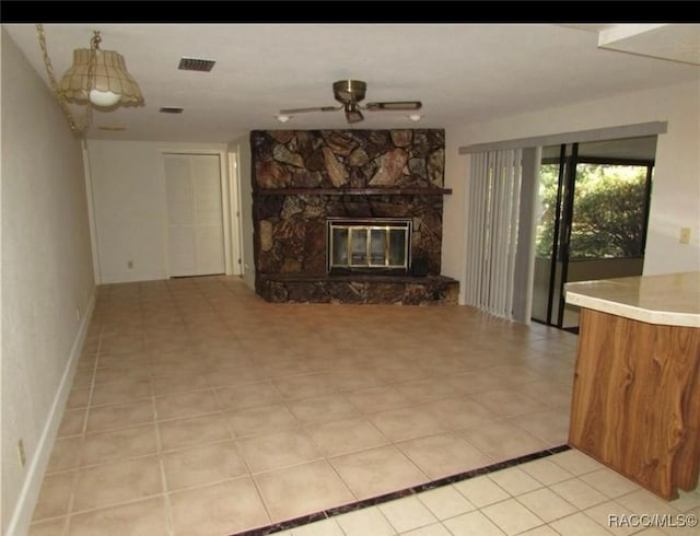 unfurnished living room with ceiling fan, a stone fireplace, and light tile patterned floors