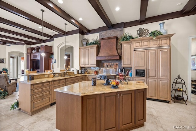 kitchen featuring premium range hood, sink, a center island, pendant lighting, and light stone countertops