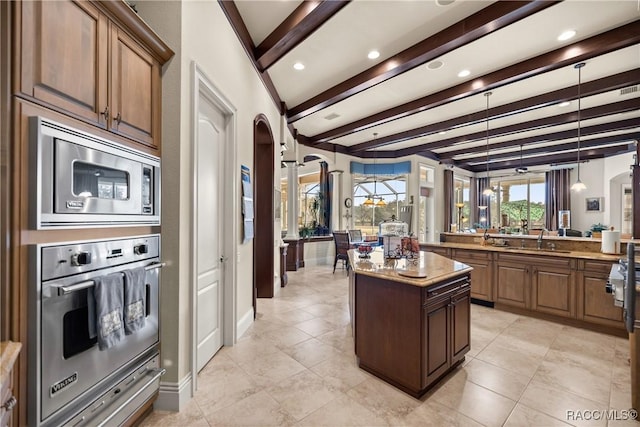 kitchen featuring appliances with stainless steel finishes, decorative light fixtures, beamed ceiling, a center island, and light stone countertops