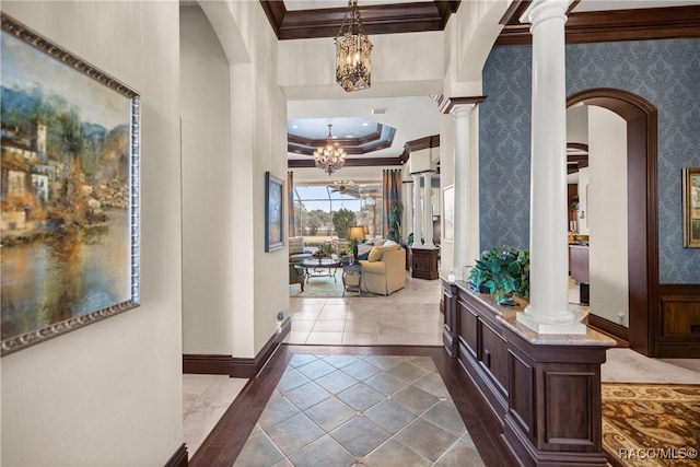 hallway featuring ornate columns, an inviting chandelier, ornamental molding, a tray ceiling, and tile patterned flooring