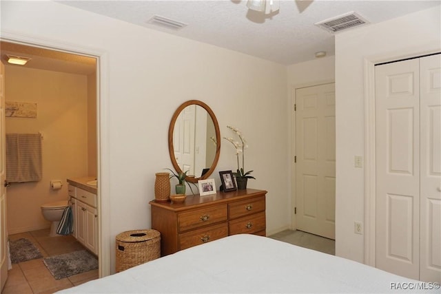 bedroom featuring light tile patterned floors, ceiling fan, ensuite bathroom, a textured ceiling, and a closet