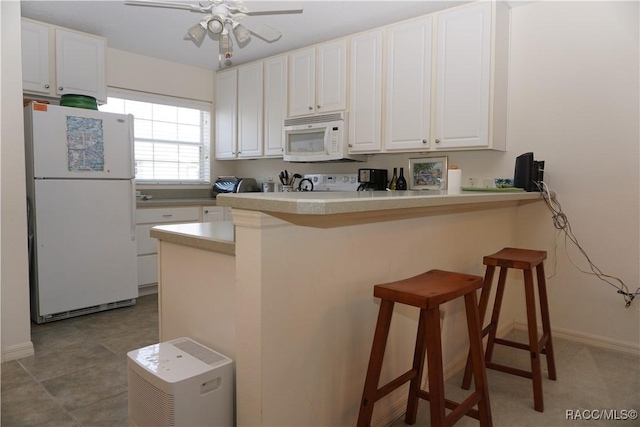 kitchen with white cabinetry, white appliances, a kitchen bar, and kitchen peninsula