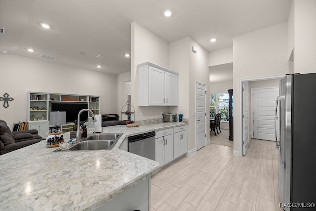 kitchen with light stone countertops, sink, kitchen peninsula, white cabinets, and appliances with stainless steel finishes