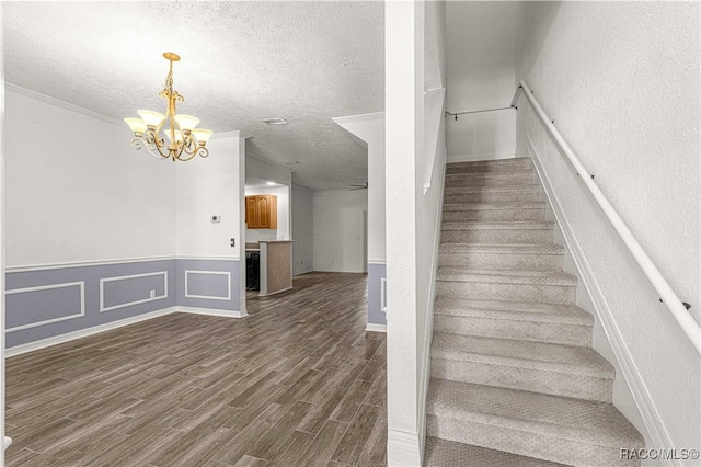 stairs with hardwood / wood-style flooring, ceiling fan with notable chandelier, ornamental molding, and a textured ceiling