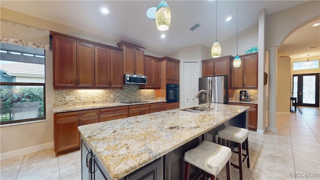 kitchen featuring decorative columns, a center island with sink, arched walkways, black appliances, and a sink