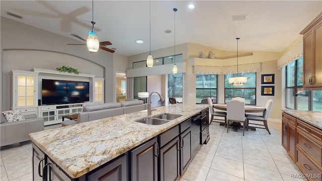 kitchen with decorative light fixtures, open floor plan, a sink, an island with sink, and light stone countertops