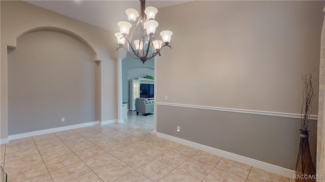 unfurnished room with arched walkways, light tile patterned flooring, a notable chandelier, baseboards, and decorative columns