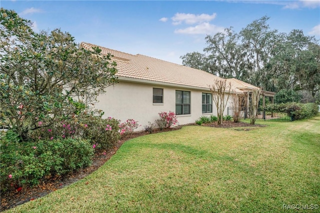 rear view of house with a tile roof, a yard, fence, and stucco siding