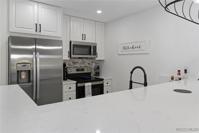 kitchen featuring white cabinets, appliances with stainless steel finishes, tasteful backsplash, and light stone counters