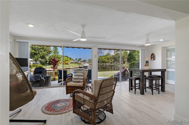 living room with light wood-type flooring, a water view, plenty of natural light, and ceiling fan