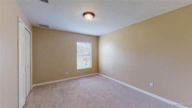 unfurnished bedroom with visible vents, light carpet, a textured ceiling, a closet, and baseboards