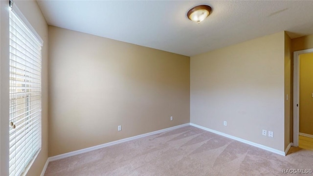 spare room featuring light carpet and baseboards