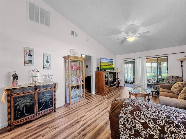 living room with ceiling fan, light hardwood / wood-style flooring, high vaulted ceiling, and a textured ceiling