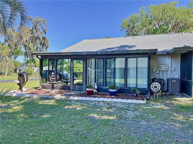 rear view of house featuring a sunroom, central AC unit, and a lawn