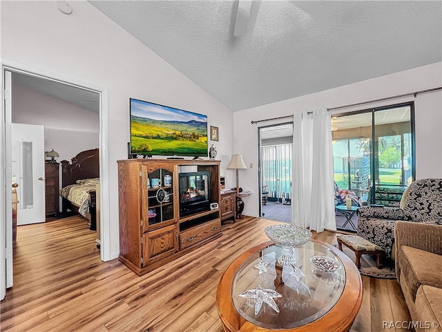 living room featuring a textured ceiling, ceiling fan, light hardwood / wood-style flooring, and vaulted ceiling