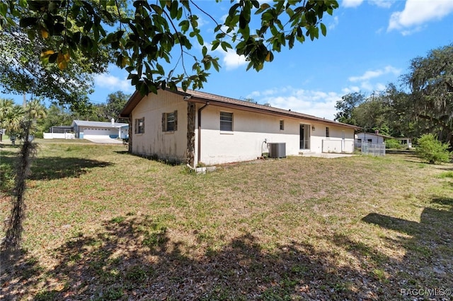 view of property exterior with fence, central AC unit, a yard, and stucco siding