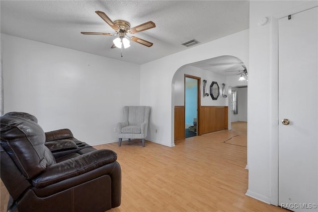 living room with ceiling fan, a textured ceiling, and light hardwood / wood-style flooring