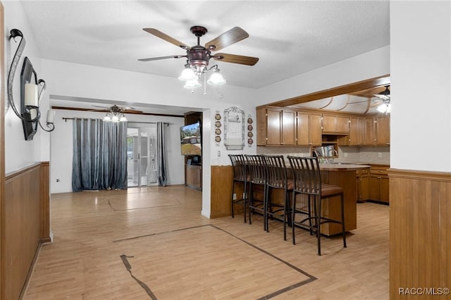 kitchen featuring a breakfast bar area, light hardwood / wood-style flooring, wooden walls, kitchen peninsula, and ceiling fan