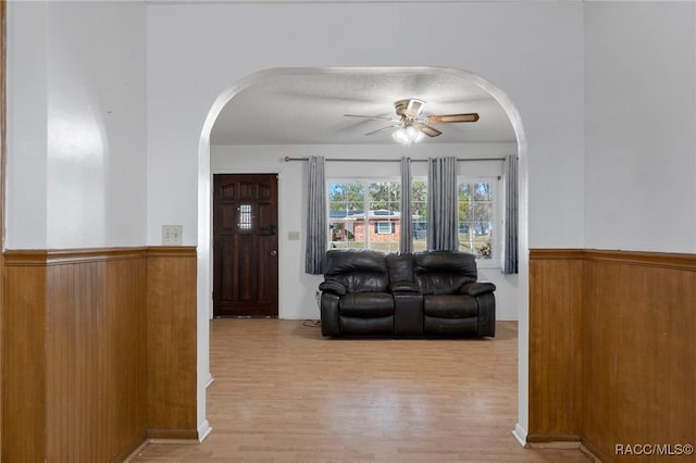 living room with light hardwood / wood-style flooring, ceiling fan, and wood walls