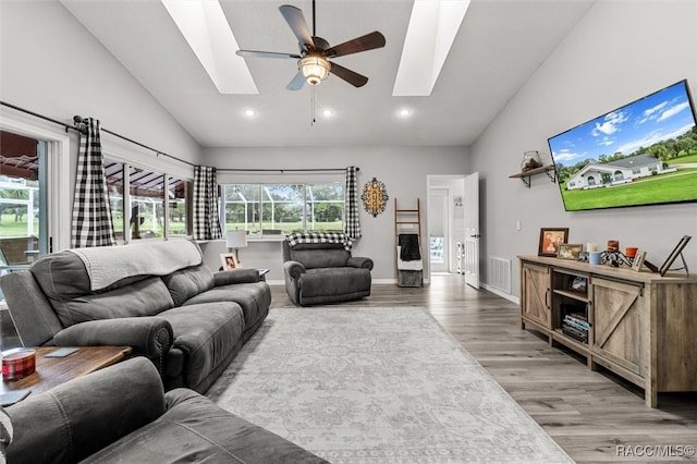 living room featuring ceiling fan, a healthy amount of sunlight, a skylight, and light hardwood / wood-style flooring