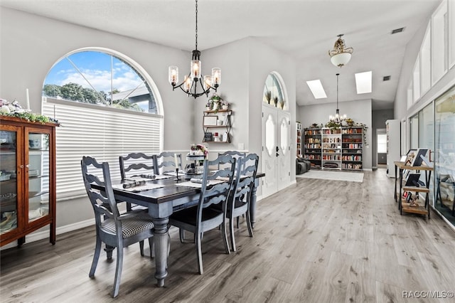 dining area featuring vaulted ceiling with skylight, a chandelier, and light hardwood / wood-style flooring