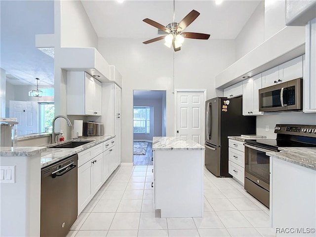 kitchen with stainless steel appliances, a center island, light stone countertops, white cabinets, and sink