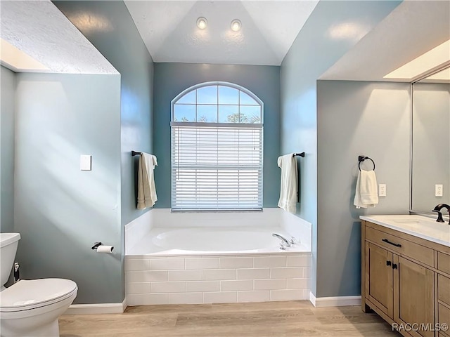 bathroom with toilet, vanity, hardwood / wood-style flooring, tiled tub, and lofted ceiling