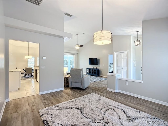 living room with ceiling fan with notable chandelier, high vaulted ceiling, and hardwood / wood-style floors