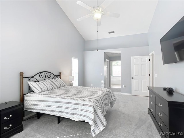 bedroom featuring ceiling fan, high vaulted ceiling, light carpet, and ensuite bath