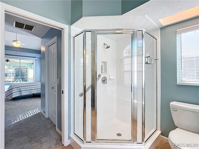 bathroom with toilet, a shower with shower door, and ceiling fan