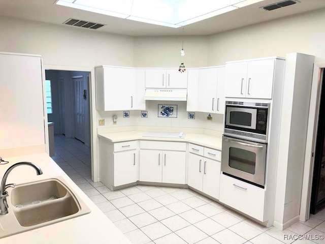 kitchen featuring built in microwave, sink, light tile patterned floors, oven, and white cabinetry