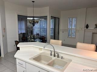 kitchen featuring sink, hanging light fixtures, light tile patterned flooring, white cabinetry, and a chandelier