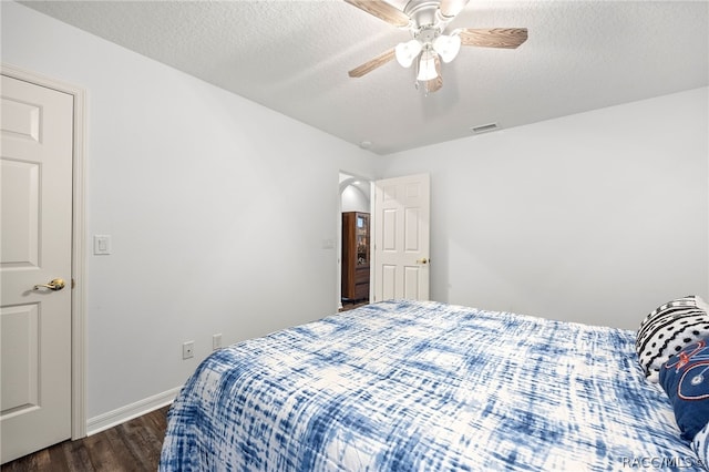 bedroom with ceiling fan, dark wood-type flooring, and a textured ceiling