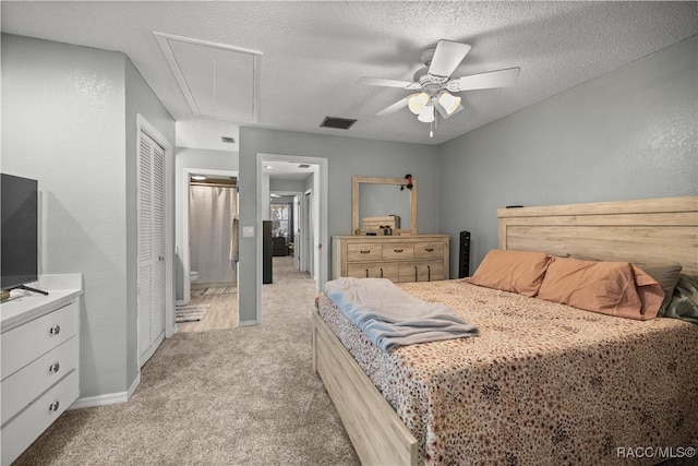 bedroom with ensuite bathroom, a textured ceiling, attic access, visible vents, and light colored carpet