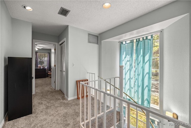 corridor with a textured ceiling, visible vents, an upstairs landing, and carpet floors
