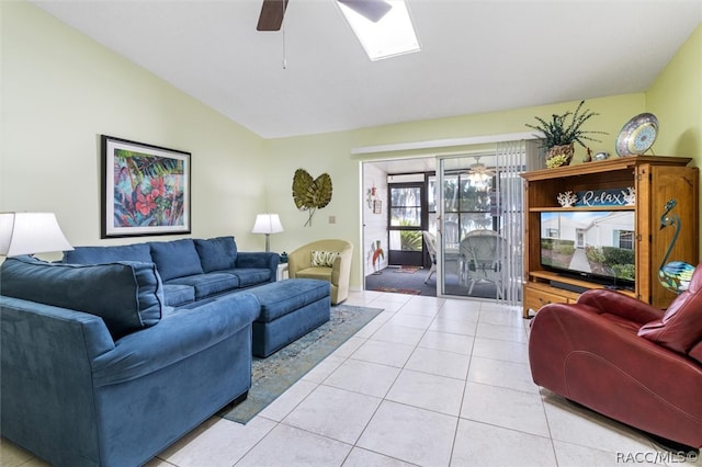 living room with ceiling fan, vaulted ceiling with skylight, and light tile patterned floors