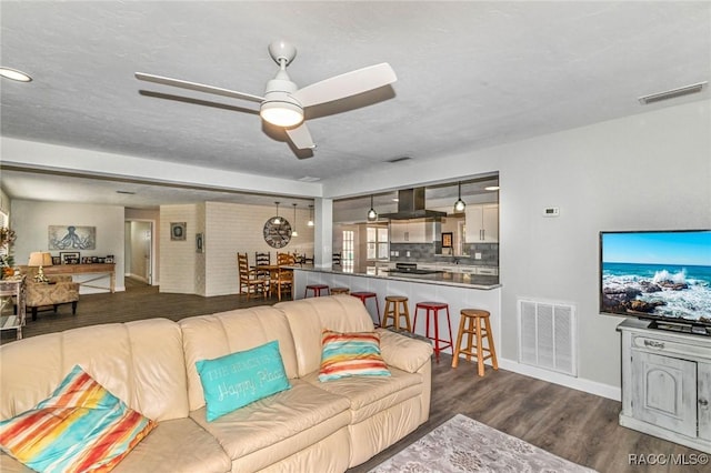 living room with dark wood-style floors, a textured ceiling, visible vents, and a ceiling fan