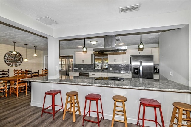 kitchen featuring a peninsula, visible vents, ventilation hood, stainless steel fridge with ice dispenser, and dark wood finished floors