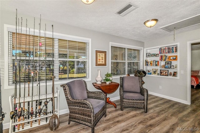 sitting room featuring attic access, visible vents, a textured ceiling, and wood finished floors