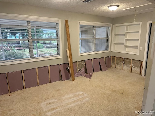 carpeted spare room with a textured ceiling, visible vents, and attic access