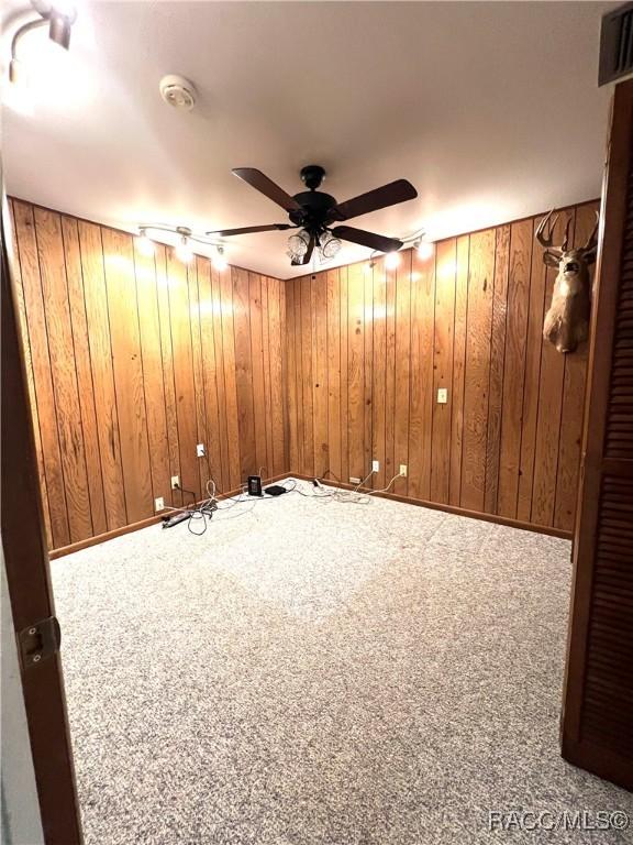 spare room featuring ceiling fan, wooden walls, and carpet