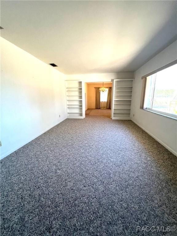 unfurnished living room with carpet floors, a healthy amount of sunlight, built in features, and an inviting chandelier